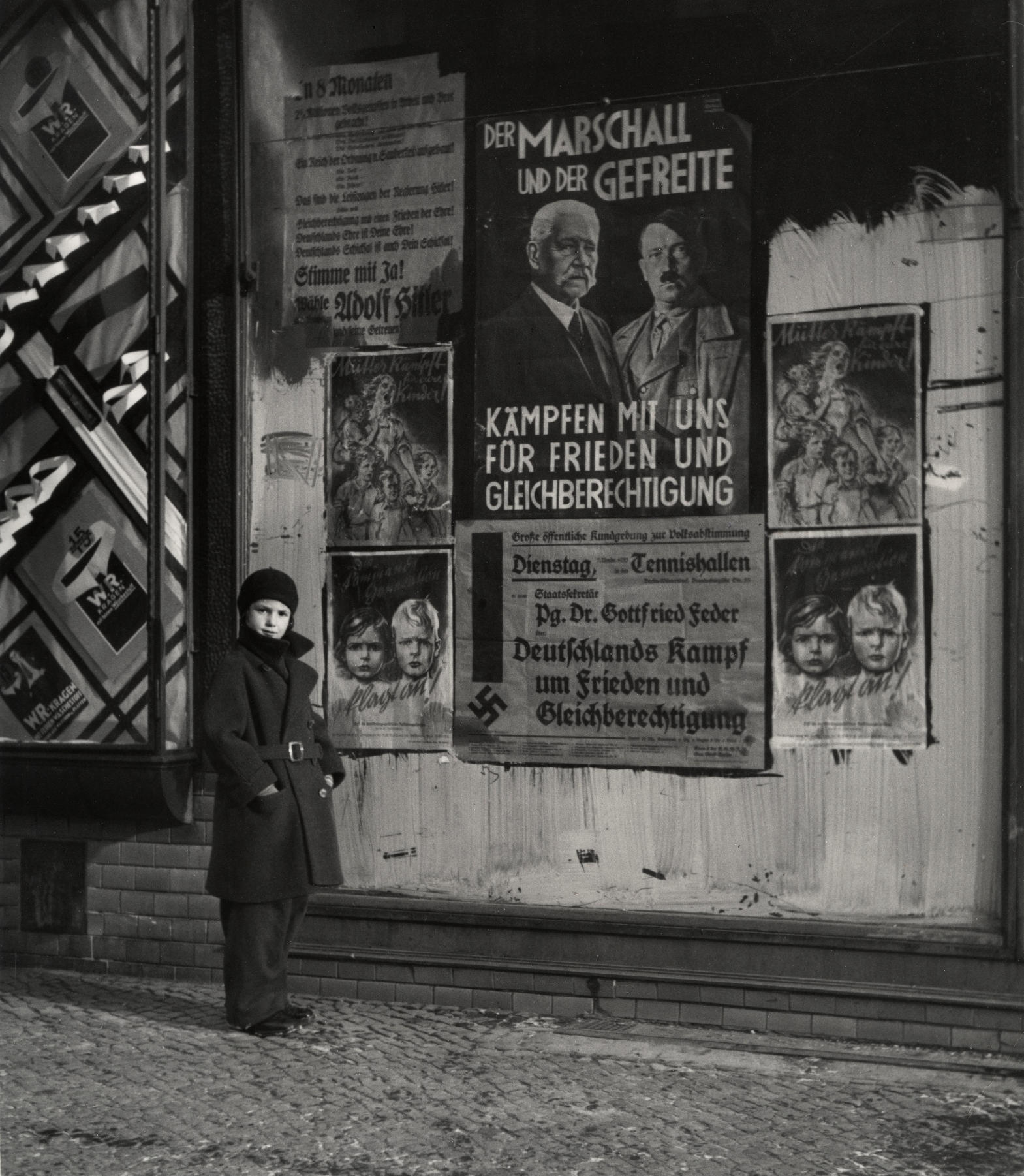 [Vishniac's daughter Mara posing in front of an election poster for Hindenburg and Hitler that reads „The Marshal and the Corporal: Fight with Us for Peace and Equal Rights” Wilmersdorf, Berlin], 1933. © Mara Vishniac Kohn, courtesy International Center of Photography (źródło: dzięki uprzejmości International Center of Photography w Nowym Jorku)