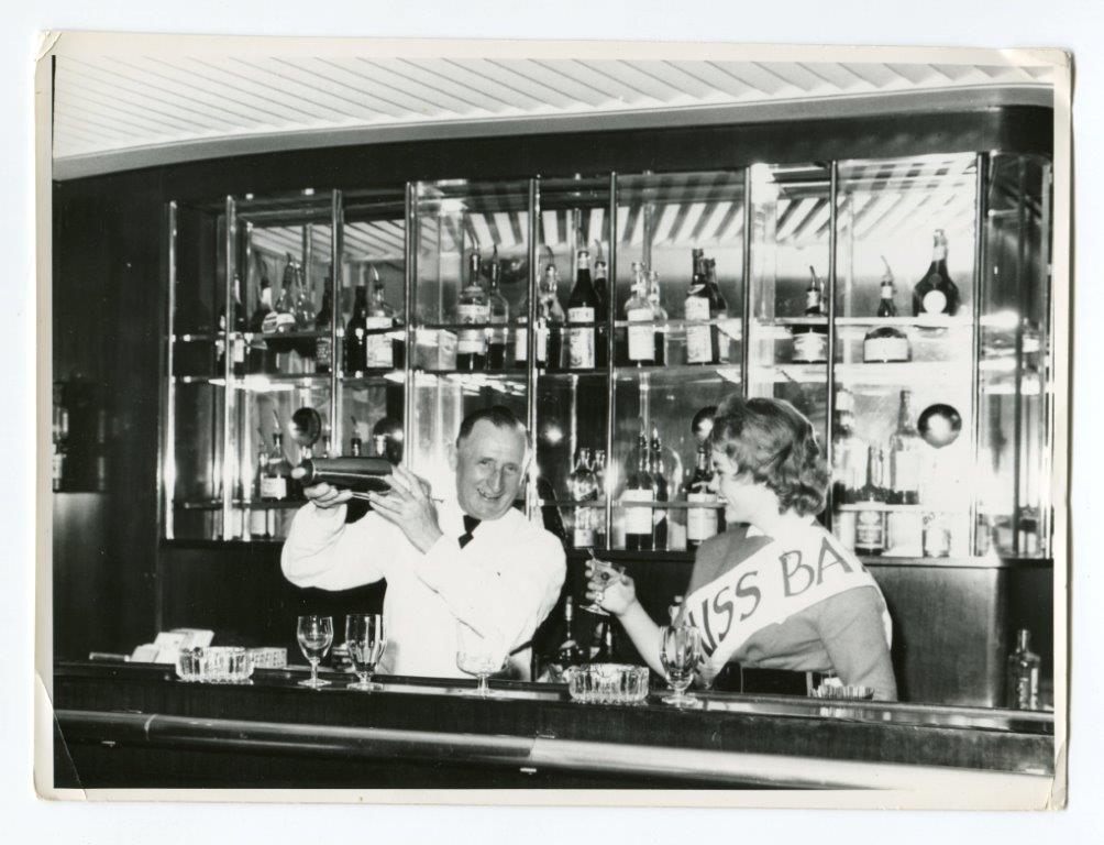 Miss m/s „Batorego” świętuje za barem w towarzystwie kelnera, przygotowujące go drinki, 1959, fot. Florian Staszewski / Muzeum Emigracji w Gdyni (źródło: materiały prasowe organizatora)